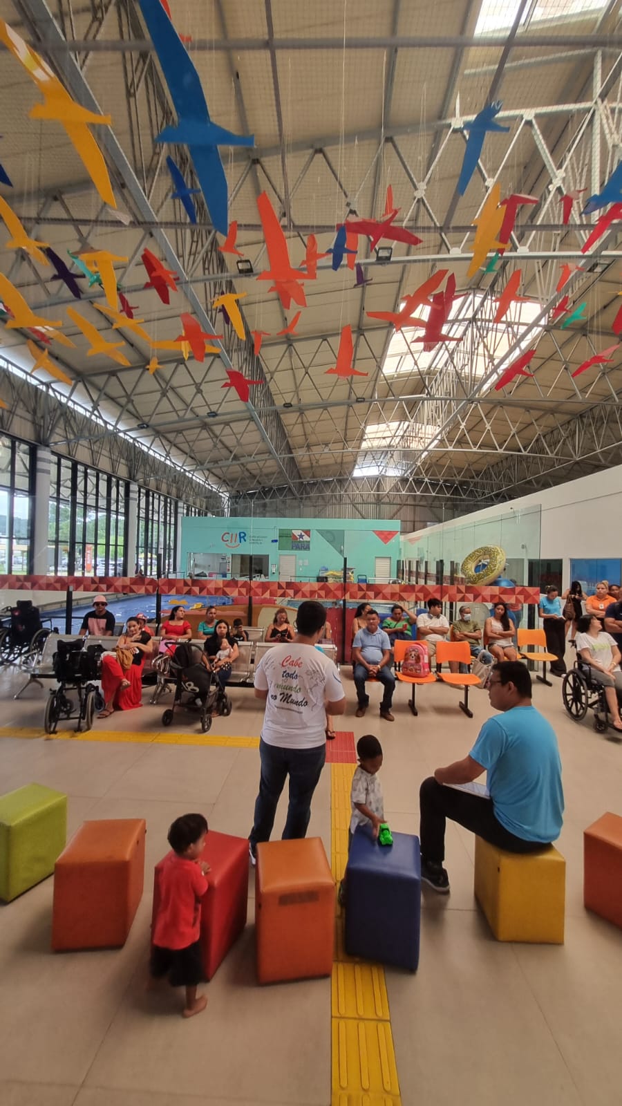 Saguão do CIIR com pássaros de papel suspensos e o público acompanhando a palestra