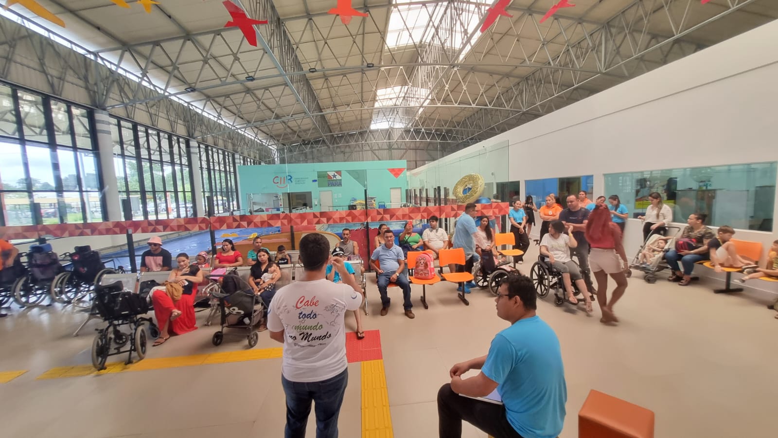 Famílias, pessoas em cadeiras de rodas e equipe reunidas no saguão do CIIR durante a palestra